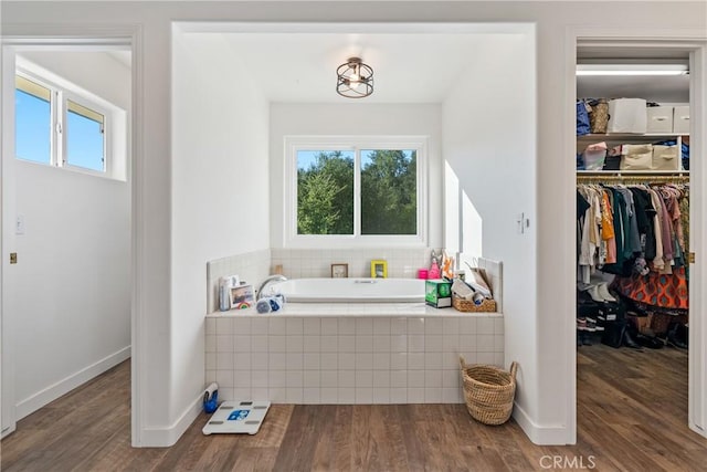 full bathroom featuring a wealth of natural light, a garden tub, a spacious closet, and wood finished floors