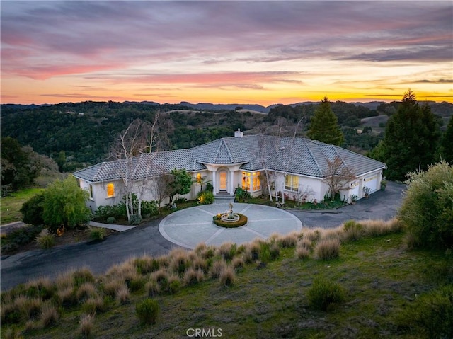 view of front of house with a chimney, curved driveway, and stucco siding