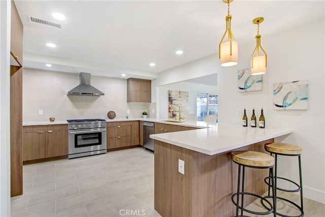 kitchen with decorative light fixtures, stainless steel appliances, kitchen peninsula, and wall chimney exhaust hood