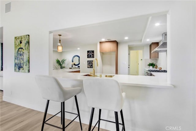 kitchen with wall chimney range hood, sink, a breakfast bar area, kitchen peninsula, and light wood-type flooring