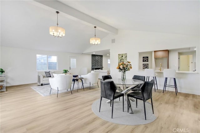 dining area featuring an inviting chandelier, vaulted ceiling with beams, light hardwood / wood-style floors, and a brick fireplace