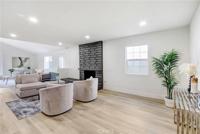 living room with lofted ceiling, a brick fireplace, and light wood-type flooring