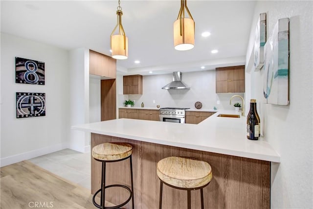 kitchen with high end stove, a kitchen bar, hanging light fixtures, kitchen peninsula, and wall chimney exhaust hood