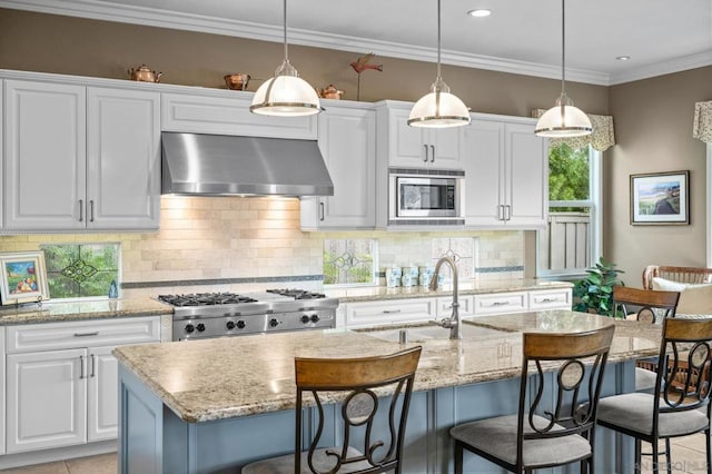 kitchen with a kitchen breakfast bar, wall chimney range hood, stainless steel microwave, and a center island with sink