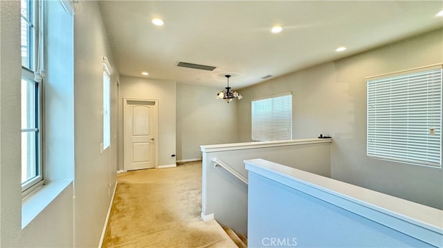 hall with light carpet and an inviting chandelier