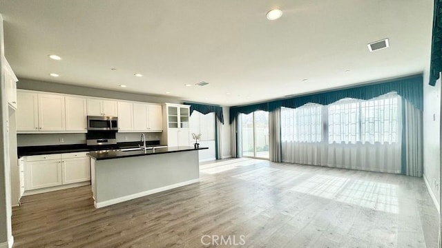 kitchen with white cabinets, wood-type flooring, sink, and a center island with sink