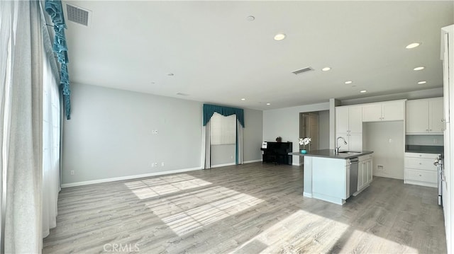 kitchen featuring dishwasher, sink, white cabinetry, light wood-type flooring, and a kitchen island with sink