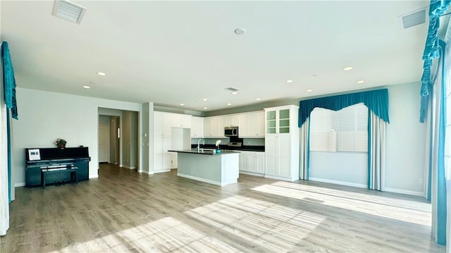 kitchen with white cabinets, fridge, an island with sink, and light hardwood / wood-style flooring