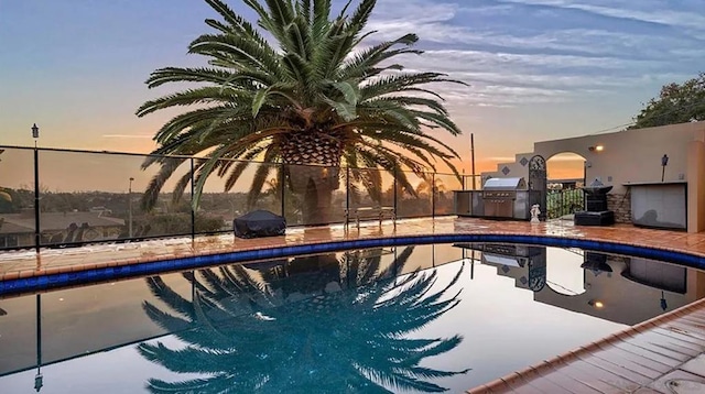 pool at dusk featuring a grill and area for grilling