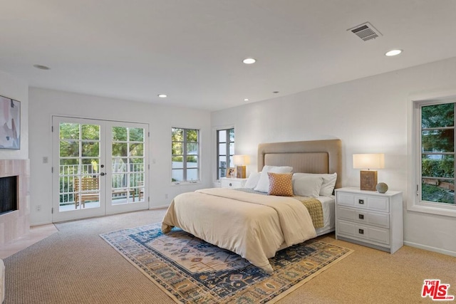 bedroom with french doors, access to exterior, light colored carpet, and a tiled fireplace