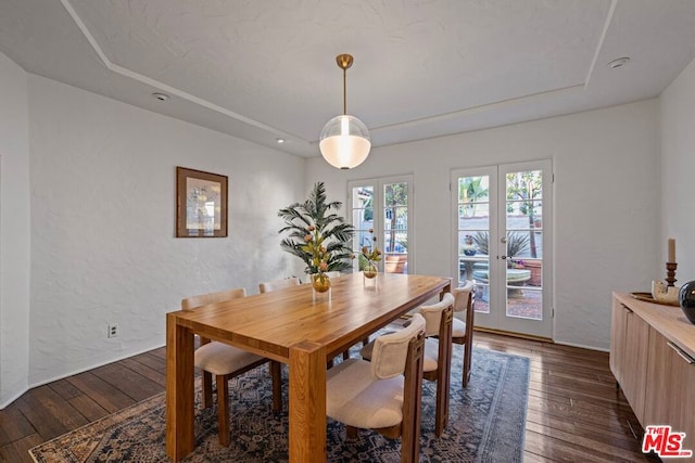 dining space with dark wood-type flooring, a raised ceiling, and french doors