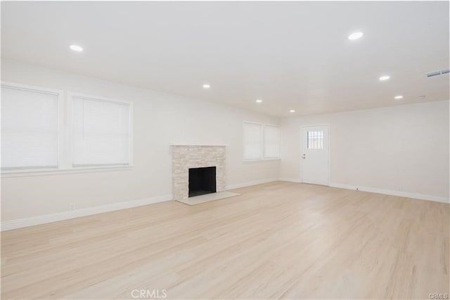 unfurnished living room with light hardwood / wood-style floors and a stone fireplace