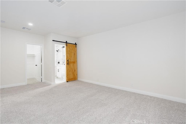 unfurnished bedroom featuring light carpet, a closet, a barn door, and a spacious closet