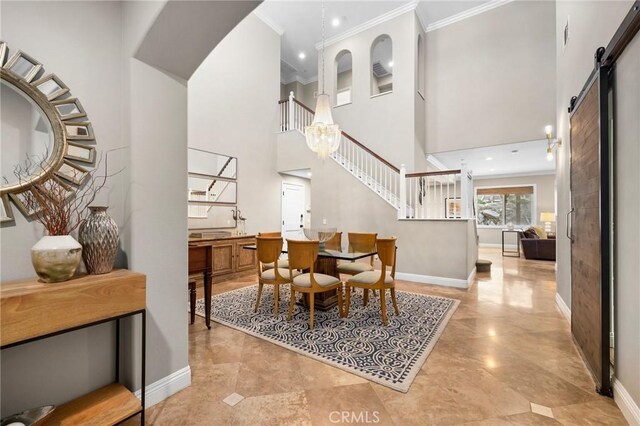 dining room featuring a high ceiling, crown molding, a barn door, and an inviting chandelier