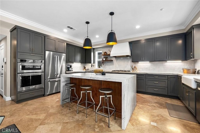 kitchen featuring custom exhaust hood, appliances with stainless steel finishes, light stone countertops, pendant lighting, and a center island