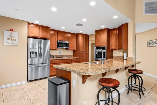 kitchen with light tile patterned flooring, appliances with stainless steel finishes, kitchen peninsula, and a breakfast bar