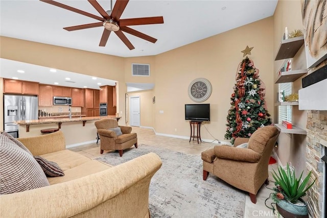 living room with a stone fireplace, ceiling fan, light tile patterned flooring, lofted ceiling, and sink