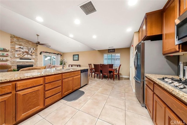 kitchen featuring ceiling fan, appliances with stainless steel finishes, lofted ceiling, a fireplace, and sink