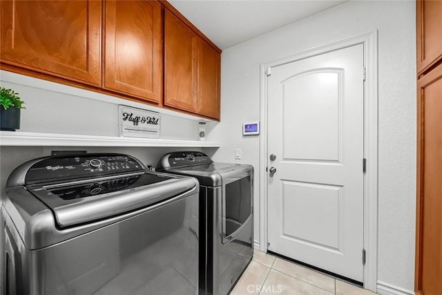 clothes washing area featuring cabinets, light tile patterned floors, and washing machine and dryer