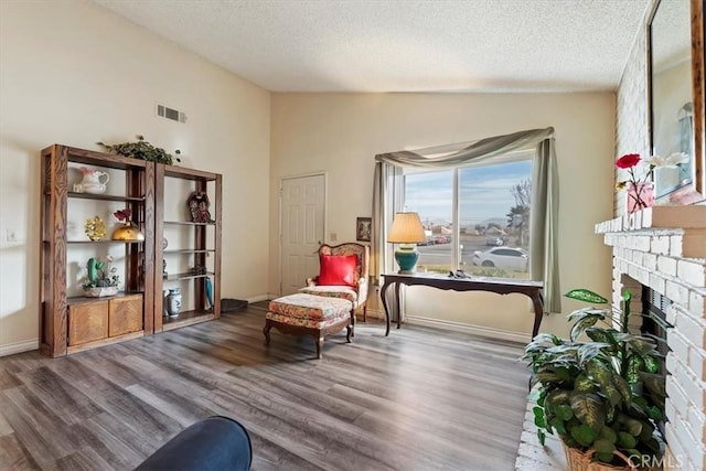 sitting room with wood-type flooring, a textured ceiling, lofted ceiling, and a brick fireplace