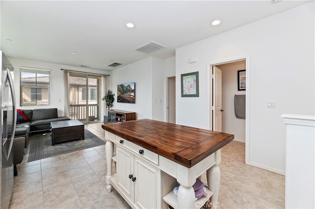 kitchen featuring stainless steel fridge, light tile patterned flooring, and white cabinetry