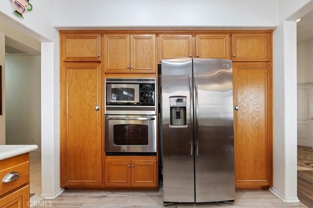kitchen featuring stainless steel appliances, light wood-type flooring, brown cabinets, and light countertops