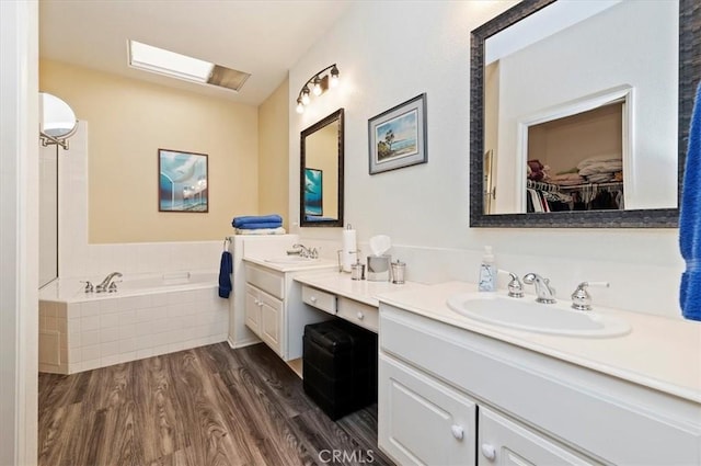 bathroom featuring a walk in closet, vanity, a bath, and wood finished floors