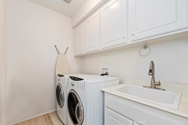 laundry area with light hardwood / wood-style floors, sink, washer and dryer, and cabinets