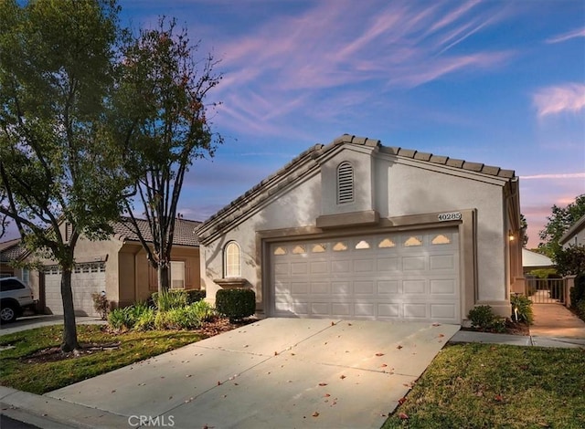 view of front of property featuring a tiled roof, an attached garage, driveway, and stucco siding