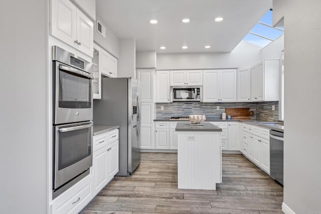 kitchen with stainless steel appliances, white cabinets, tasteful backsplash, light hardwood / wood-style flooring, and a kitchen island