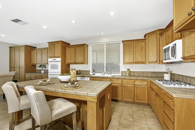 kitchen with tile counters, white appliances, light tile patterned flooring, a kitchen island, and a breakfast bar