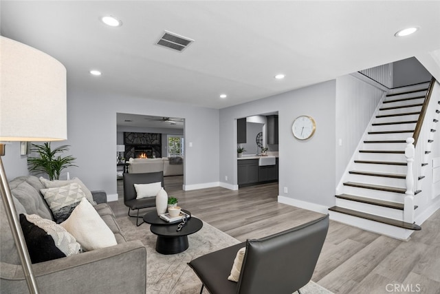 living room with ceiling fan, a high end fireplace, and light hardwood / wood-style flooring