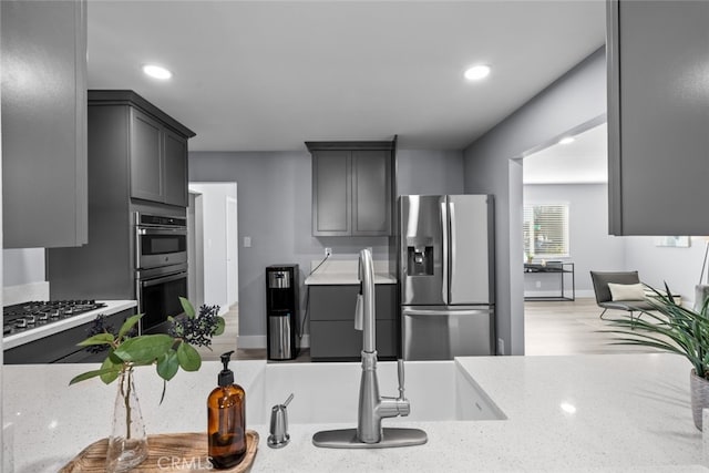 kitchen with light stone counters, appliances with stainless steel finishes, and gray cabinetry