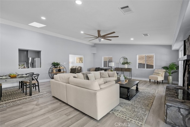 living room with a skylight, ceiling fan, and light hardwood / wood-style flooring