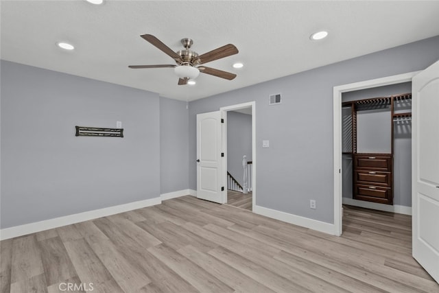 unfurnished bedroom with ceiling fan, a walk in closet, light hardwood / wood-style floors, and a closet