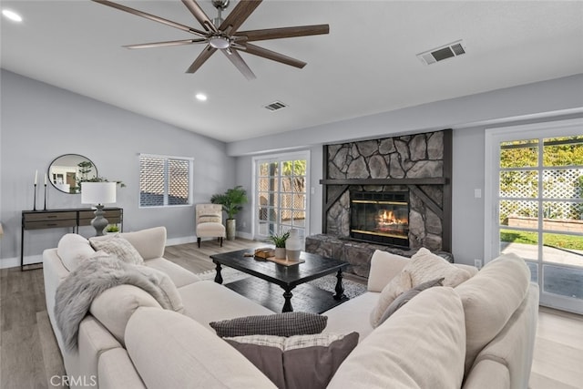 living room featuring light wood-type flooring, a fireplace, a healthy amount of sunlight, and vaulted ceiling