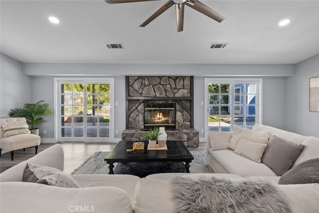 living room with hardwood / wood-style floors, a stone fireplace, and ceiling fan