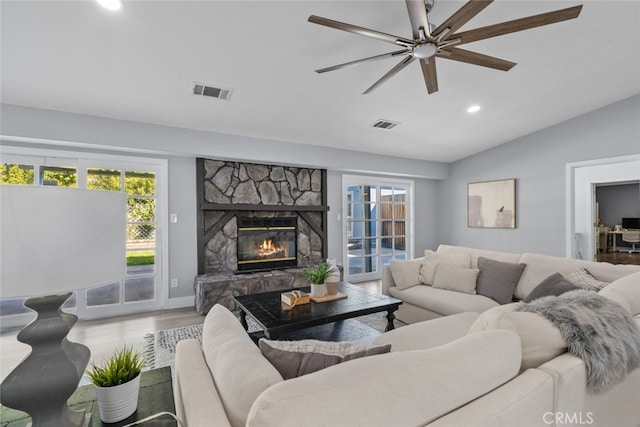 living room with hardwood / wood-style flooring, ceiling fan, a stone fireplace, and vaulted ceiling