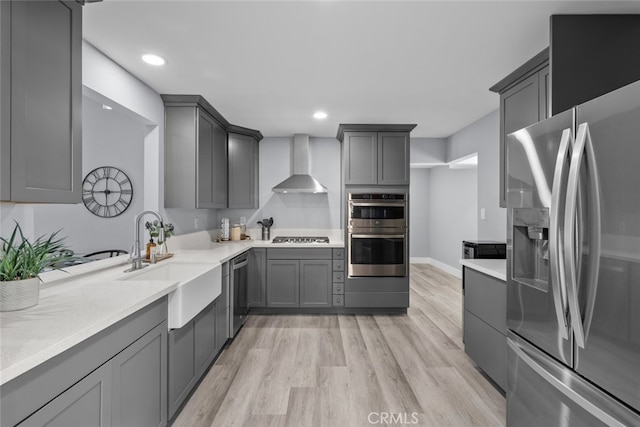 kitchen featuring sink, gray cabinetry, stainless steel appliances, wall chimney range hood, and light wood-type flooring