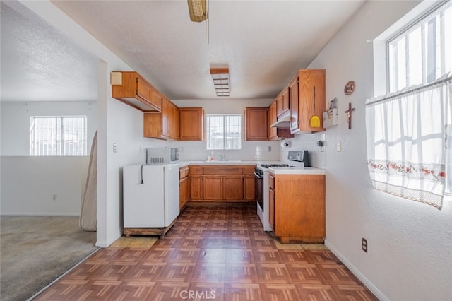 kitchen with dark colored carpet, backsplash, white gas stove, a textured ceiling, and sink