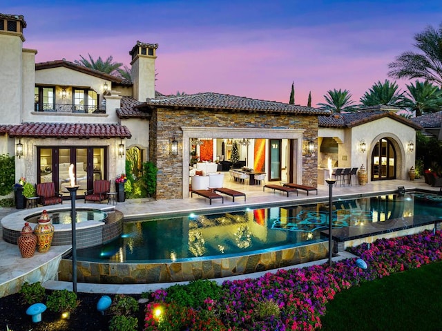 back house at dusk featuring a balcony, an outdoor living space, a pool with hot tub, and a patio area