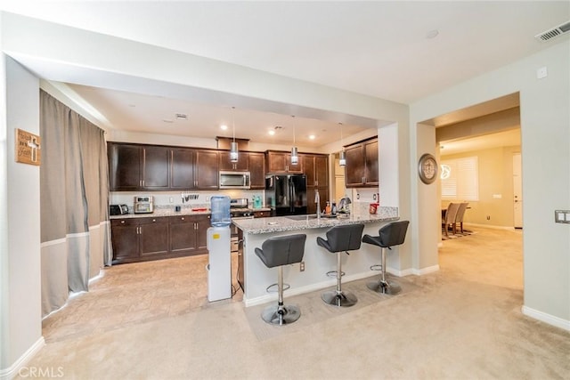 kitchen with stainless steel appliances, decorative light fixtures, a kitchen breakfast bar, light colored carpet, and light stone counters