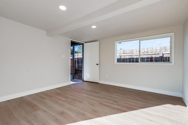 empty room with a healthy amount of sunlight, light hardwood / wood-style floors, and beamed ceiling