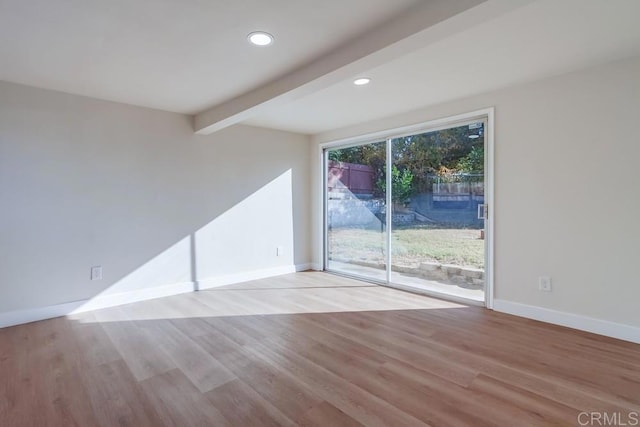 empty room featuring a healthy amount of sunlight, light hardwood / wood-style flooring, and lofted ceiling with beams