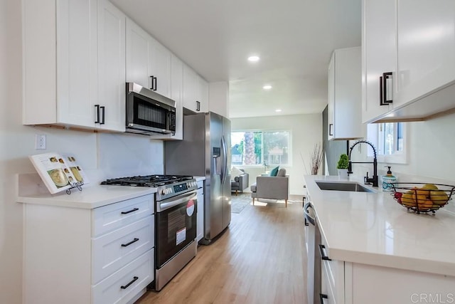 kitchen featuring appliances with stainless steel finishes, sink, white cabinetry, and light hardwood / wood-style flooring