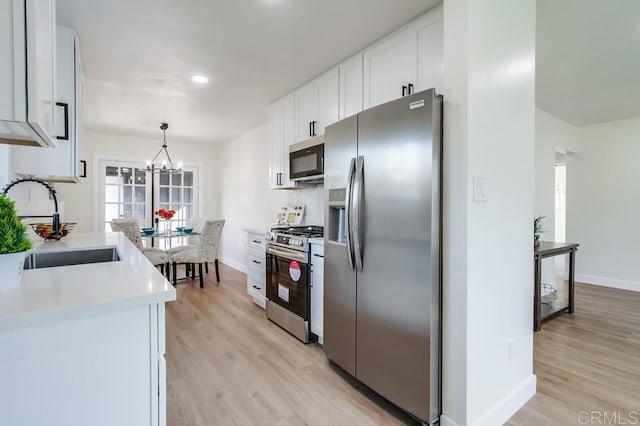 kitchen with pendant lighting, appliances with stainless steel finishes, white cabinetry, a chandelier, and light hardwood / wood-style flooring