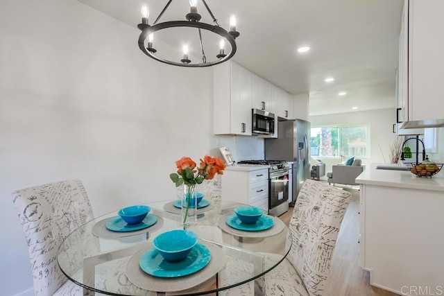 kitchen with sink, white cabinetry, light hardwood / wood-style flooring, stainless steel appliances, and a chandelier