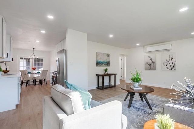 living room featuring sink, a wall unit AC, a notable chandelier, and light wood-type flooring