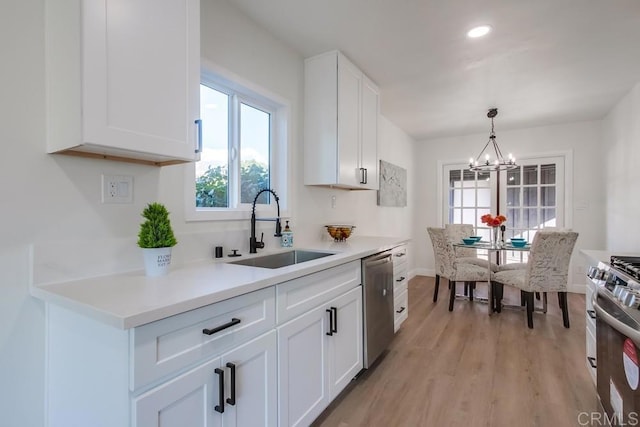 kitchen featuring white cabinetry, stainless steel appliances, light hardwood / wood-style floors, sink, and a chandelier