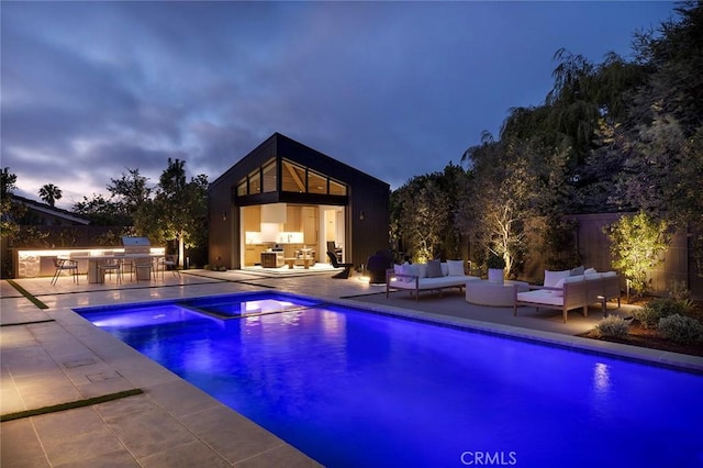 pool at dusk featuring an outdoor kitchen, an outdoor hangout area, and a patio